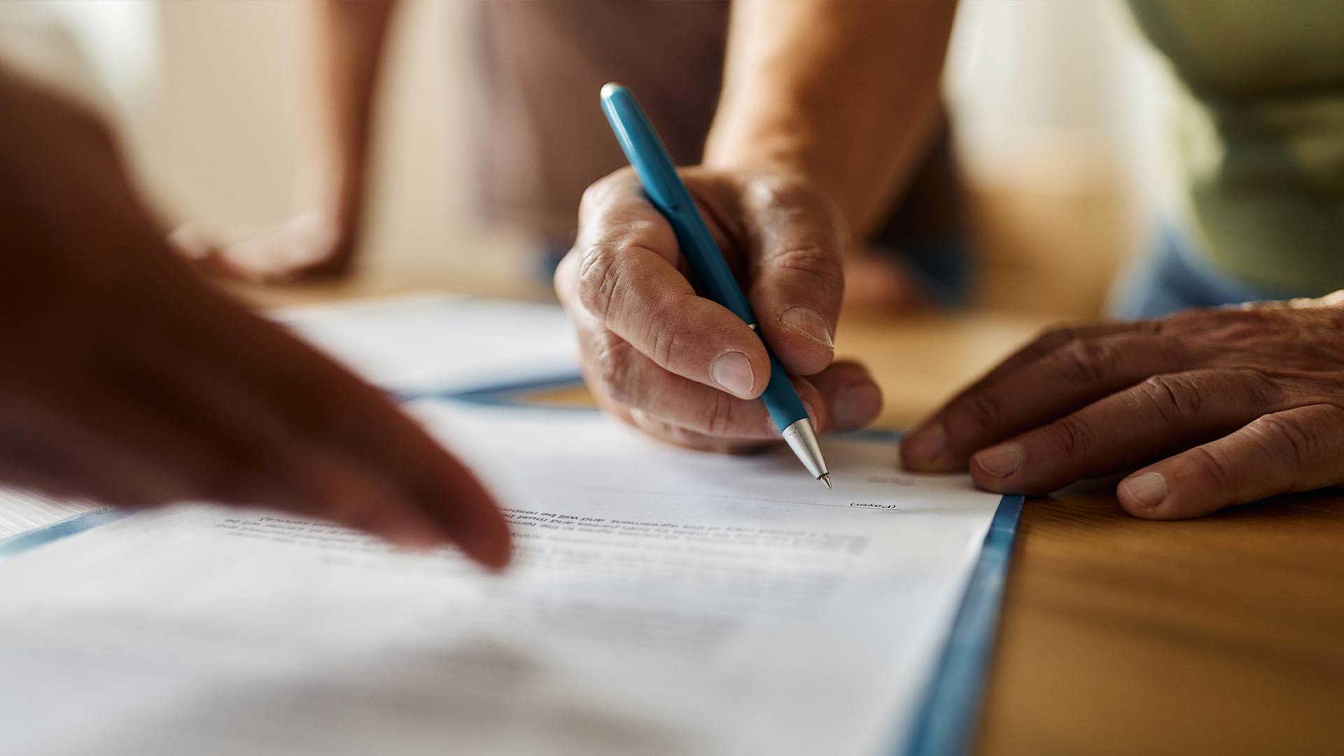 Close up of white sheet documentation. A person can be seen writing with a pen. 