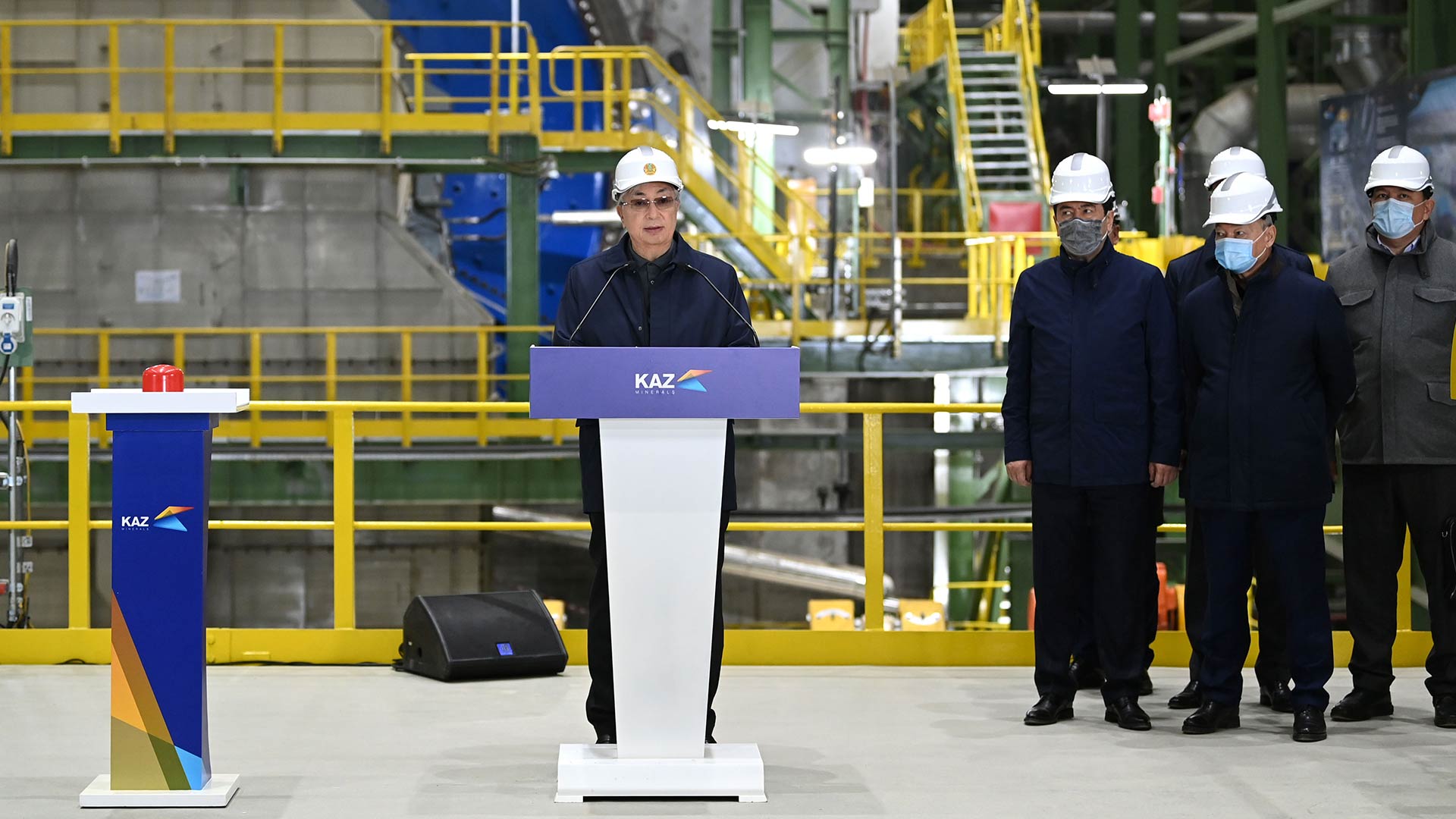 Kaz Minerals worker see talking and standing at podium. To the right in the background are four other workers watching on.
