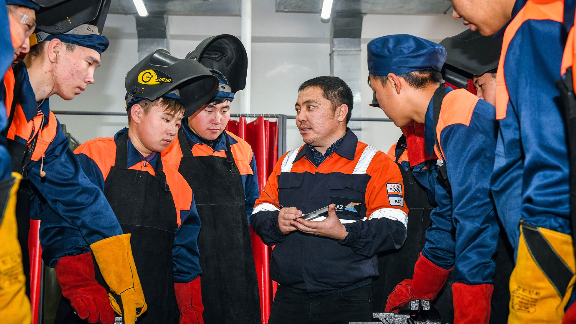 Multiple workers gathered around having a discussion. They are wearing protective clothing and headwear.