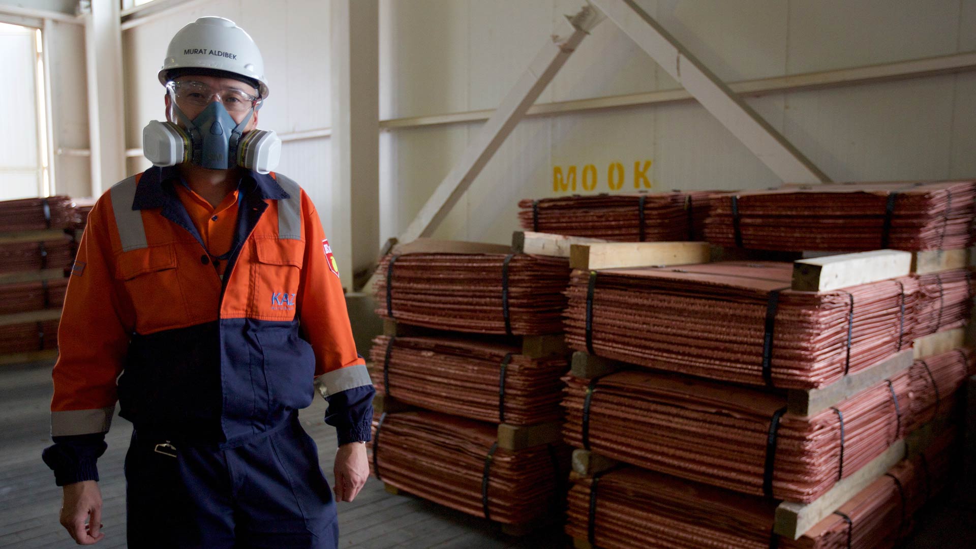 Person in safety gear looking at the camera. Materials are stacked in the background. 