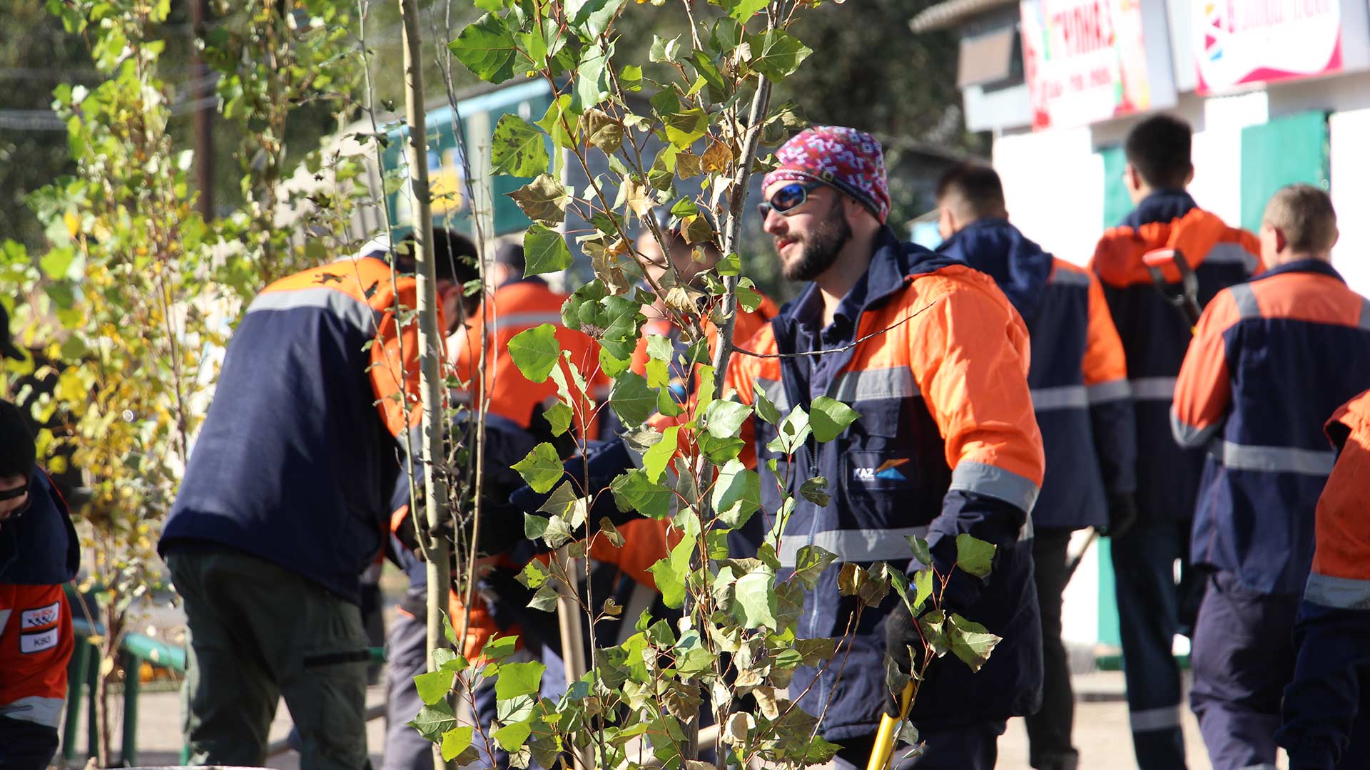 A group of workers in orange and navy uniforms plant trees. 