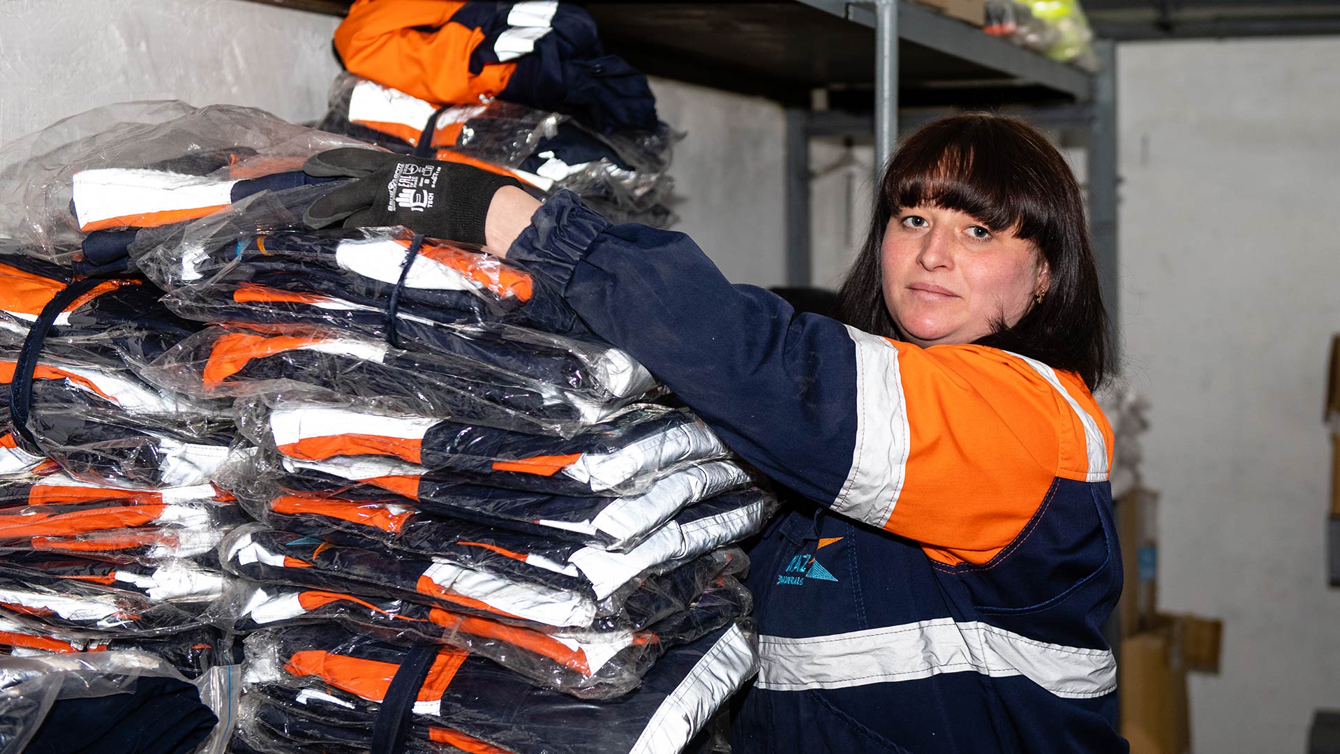 Person in safety gear looking at the camera. Machinery is visible in the background. 